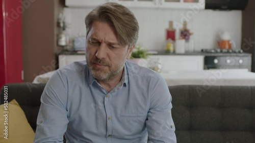 Unhappy man feels uncomfortable while using smartphone. Angry man having problem with cell phone texting. The male user sitting on the sofa at home was frustrated by what the smartphone saw.