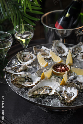 Fresh oysters on a platter in ice with a slice of lemon and spicy sauce.