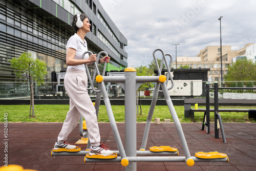 One woman modern mature caucasian female with short hair training in front of building in day on orbitrack elliptical trainer machine simulator at outdoor gym Sport fitness healthy lifestyle concept photo