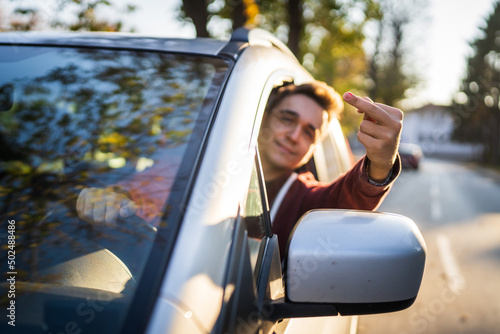 close up on hand with middle finger rude gesture showing by young adult man driving the car angry frustrated