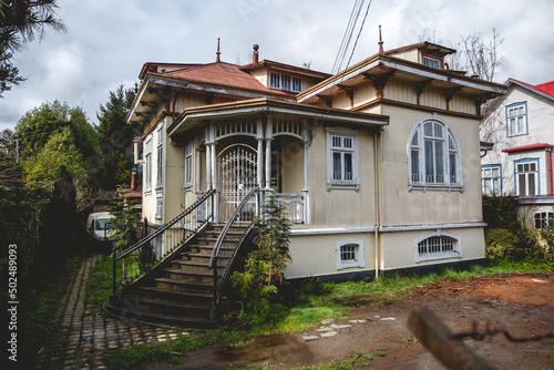 Three story old centuries cream wood house with stone basement and green garden with in a cloudy day, Valdivia, Chile