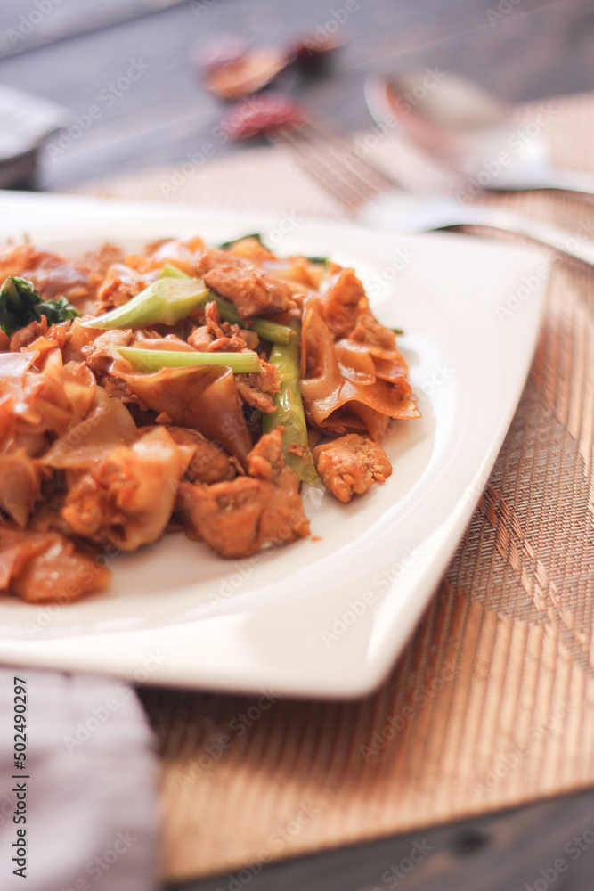 Stir fried Noodle with black soy sauce served in a white plate. on the black wooden table or what we call Stir fried Noodle with black soy sauce served in a white plate. on the black wooden table or what we call