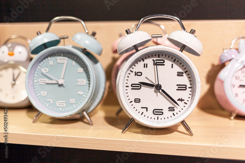 Round alarm clock on the store shelf close-up. Sale of various watches and alarm clocks of different colors. Retro alarm clock on the table, vintage tone.