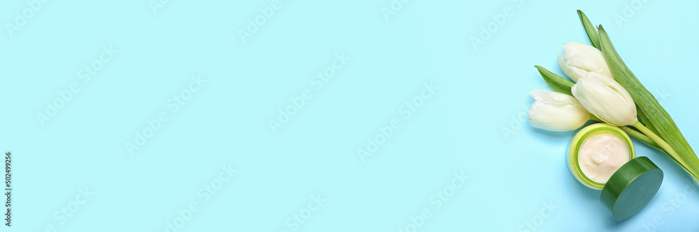 Beautiful white tulips and jar of facial cream on blue background with space for text Beautiful white tulips and jar of facial cream on blue background with space for text