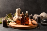 Wooden board with bottles of essential oil, sea salt, massage bag and burning candles on dark background