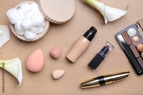 Composition with decorative cosmetics, makeup sponges, cotton balls and calla lilies on color wooden background