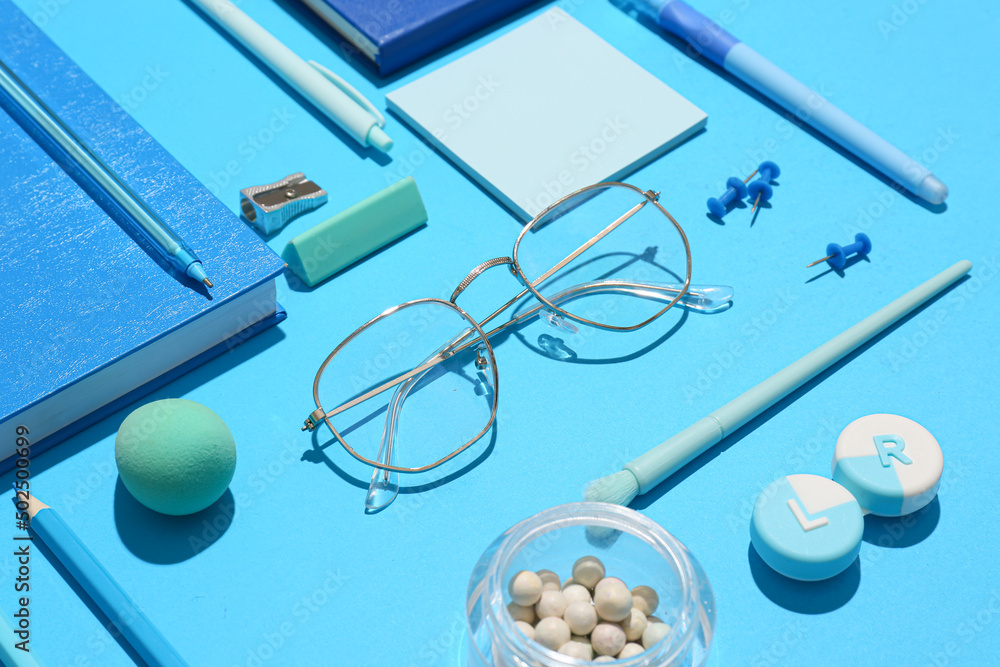 Stylish eyeglasses with stationery and cosmetic products on blue background Stylish eyeglasses with stationery and cosmetic products on blue background