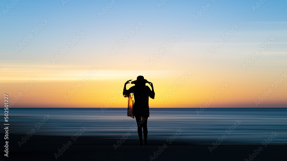 Silhouette of a woman in the sea with a beach hat at sunset.