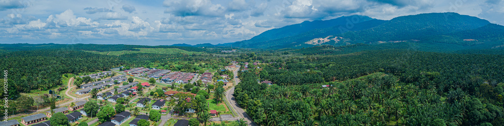 Panoramic aerial drone view of oil palm plantations land and workers settlements in Asahan, Melaka, Malaysia.