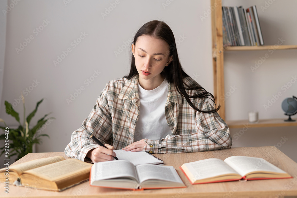 Asian female student studying remotely from home taking notes. Teenage student learning distance with books doing homework. Asian female student studying remotely from home taking notes. Teenage student learning distance with books doing homework.