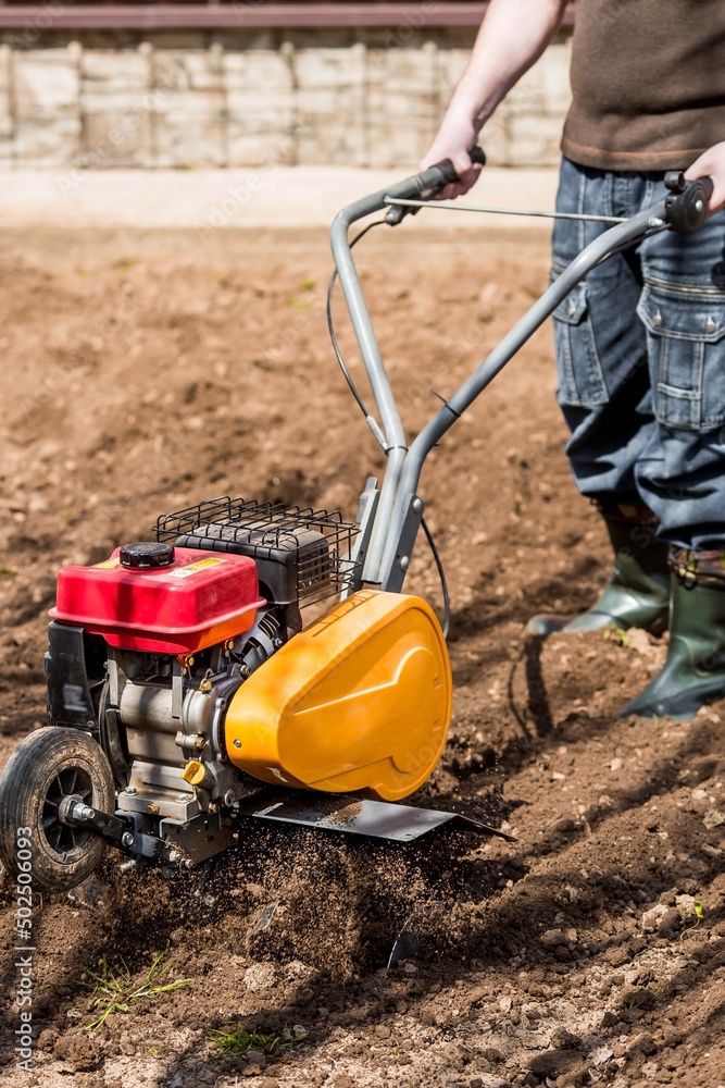 Obraz premium Banner. A male farmer plows the land with a cultivator. Agricultural machinery for tillage in the garden, combine harvester.