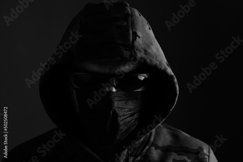 Stylish man in dark hoodie with black glasses and mask dark background, hacker, attacker and bandit.