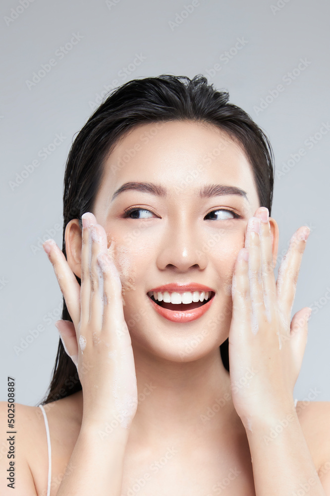 Portrait of cheerful laughing Asian woman applying foam for washing on her face with attractive appearance. Skincare spa relax concept. Isolated on grey background Portrait of cheerful laughing Asian woman applying foam for washing on her face with attractive appearance. Skincare spa relax concept. Isolated on grey background