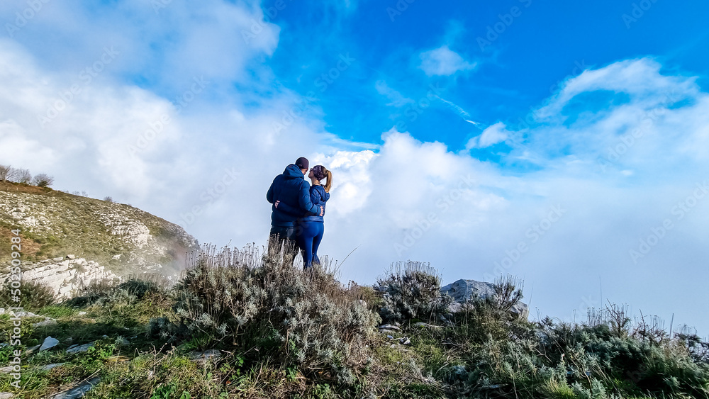 Couple with scenic view from Monte Comune on thick white clouds and blue sky near coastal town Positano. Magical hiking above fog in Lattari Mountains, Apennines, Amalfi Coast, Campania, Italy, Europe