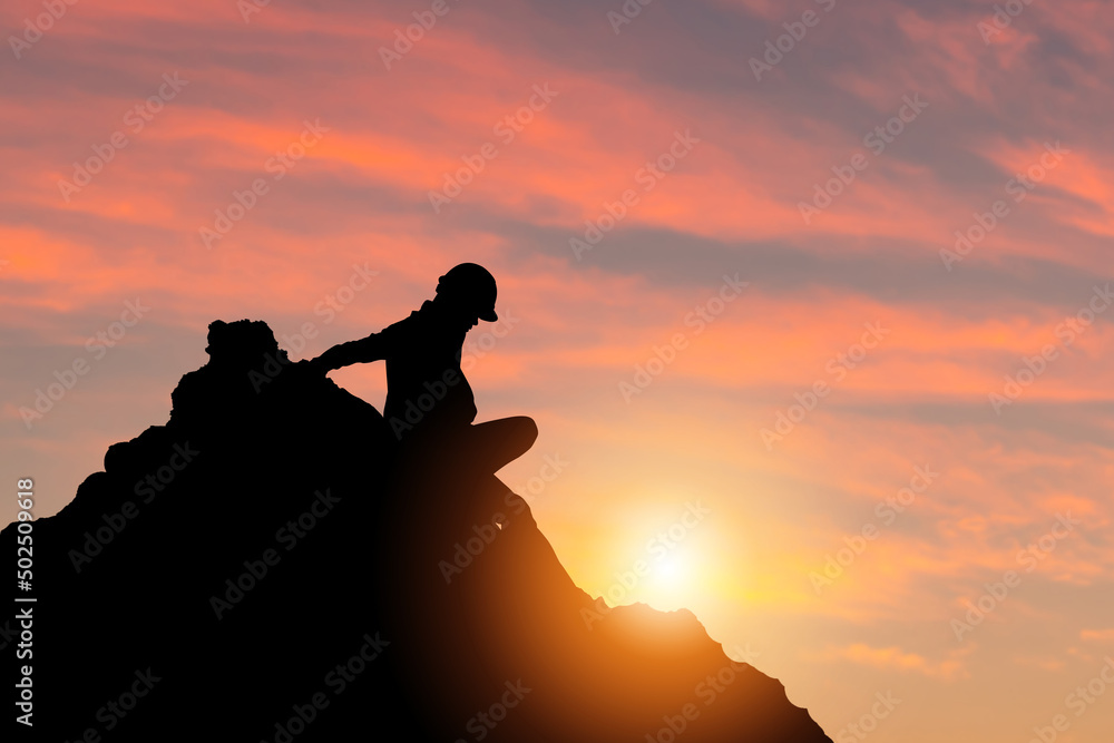 Silhouette of engineer man in hard hat on a mountain top sunset sky background