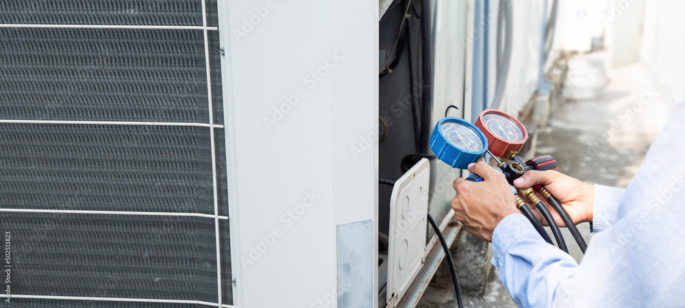 Air repair mechanic using measuring equipment for filling industrial factory air conditioners and checking maintenance outdoor air compressor unit.