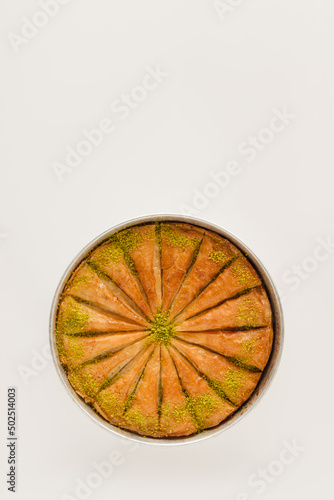 Sweet pastry - baklava cut into slices, stands in a round tray on an isolated pastel beige background with copy space. Note card for traditional baked dessert. Minimal concept of delicious food.