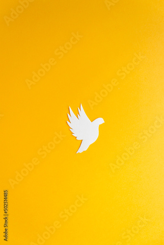 White paper dove bird as a symbol of peace isolated on yellow background. Peace to Ukraine. International Day of Peace.
