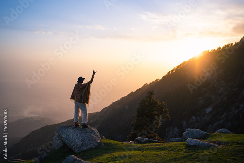 Silhouette of person stand on peak of mountain with hands raised up on sunset, Triund Trek, Himachal Pradesh, India.