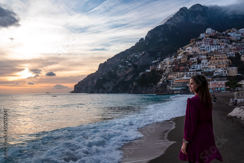 Tourist woman watching sunset on sandy Fornillo Beach and colorful buildings of hillside village Positano at Amalfi Coast, Italy, Campania, Europe. Luxury vacation at Tyrrhenian, Mediterranean Sea © Chris