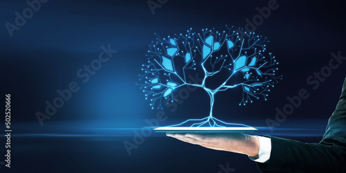 Close up of businessman hand holding smartphone with glowing digital polygonal tree on blue background with mock up place. Network, technology and database concept. photo