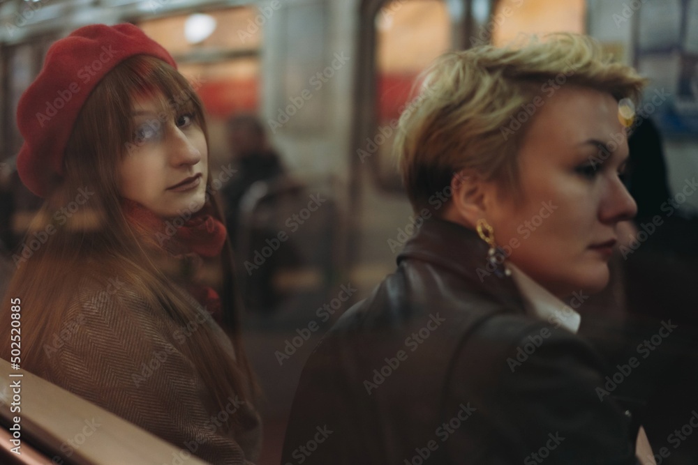 caucasian girls sitting in a car of saint petersburg metro. View from platform through glass. Image with selective focus and reflection