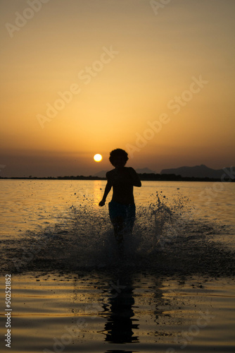 Natural reserve of the Stagnone or natural reserve of the Saline dello Stagnone near Marsala and Trapani, Sicily, Italy, silhouette of person moving in the shallow water at sunset
