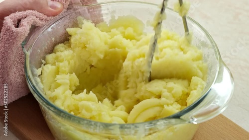 Mashing potato with butter or milk using stainless steel potato masher in a glass pot, close up. photo
