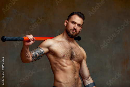 A fighter or karate man, stands in a fighting artificially pose and holds a bamboo stick on gray wall studio background.