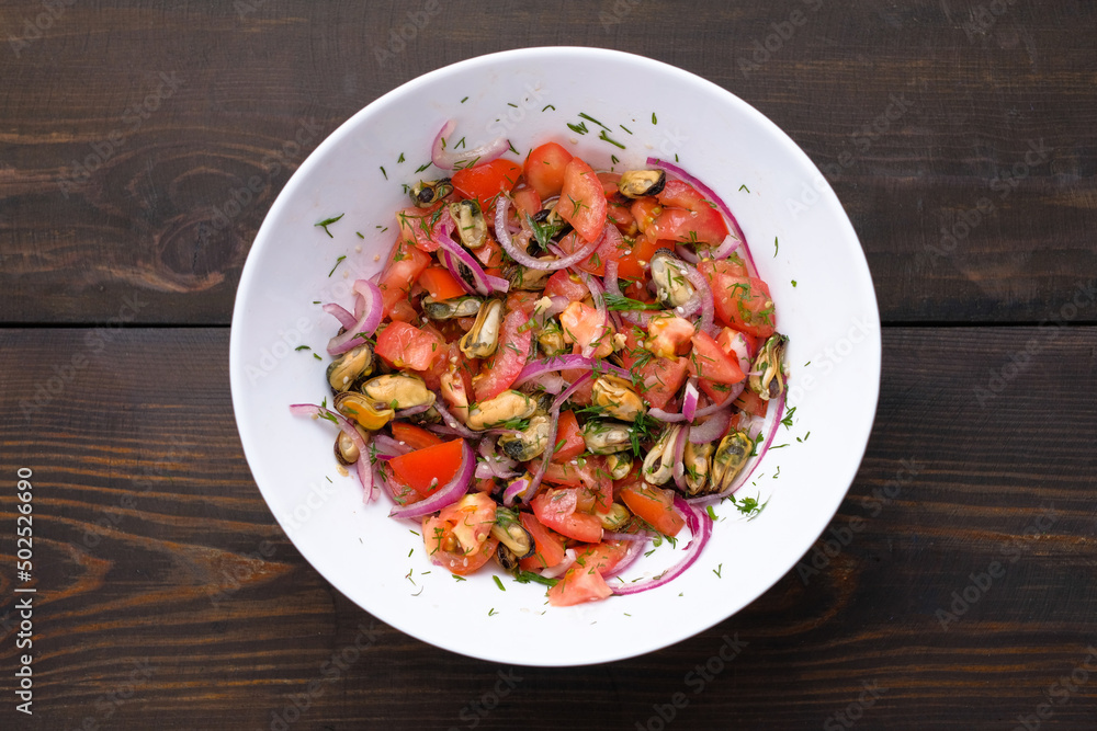 Salad with mussels and tomatoes and red onion in white plate on wooden table. Concept of healthy diet food. Flat lay. Salad with mussels and tomatoes and red onion in white plate on wooden table. Concept of healthy diet food. Flat lay.