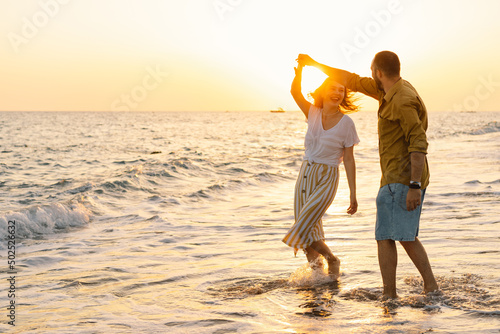 Young romantic couple dancing turning around by sea. Seascape at sunset with beautiful sky. Romantic couple on the beach at golden sunset. Lover couple having fun on beach.