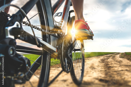 Foot on bike pedal at sunset. Close up rear view cyclist pedalling. Bicycle on the road.
