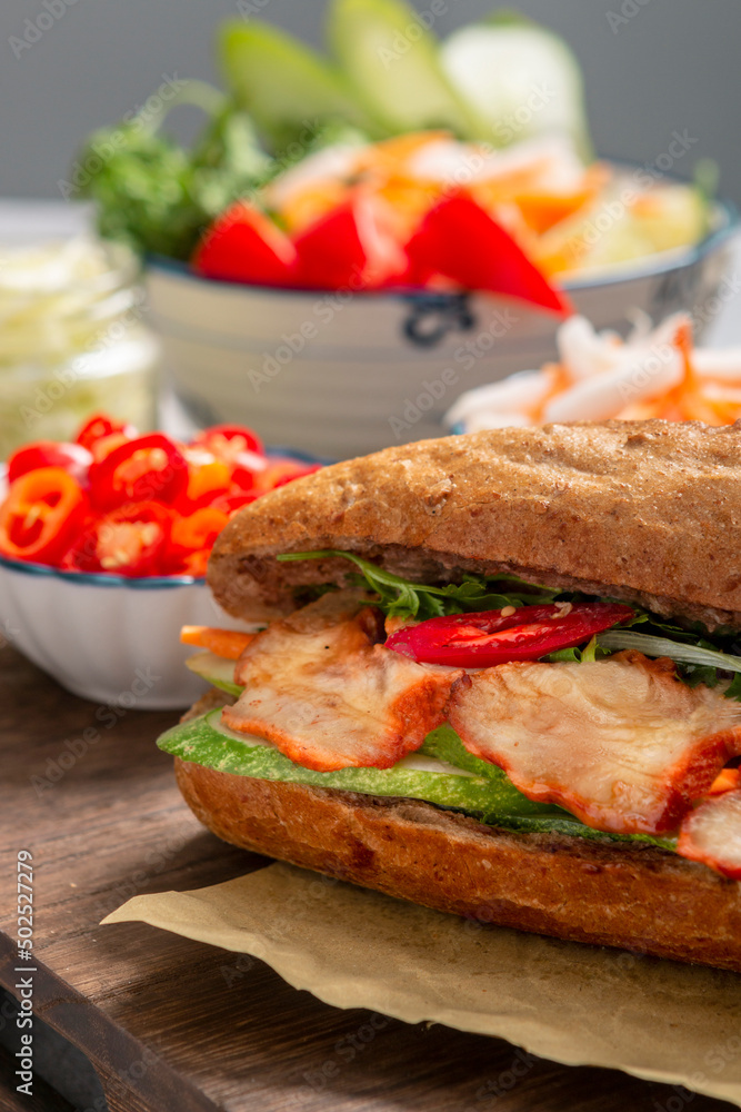 Banh Mi - Vietnamese sandwich with sausage, pork, lettuce, tomato and arugula on the light grey texture background. One of the most famous street food in the world Banh Mi - Vietnamese sandwich with sausage, pork, lettuce, tomato and arugula on the light grey texture background. One of the most famous street food in the world