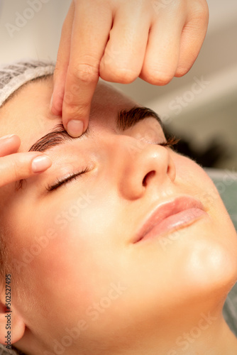 Eyebrow massage. Beautiful caucasian young white woman receiving an eye and eyebrow massage with closed eyes in a spa salon