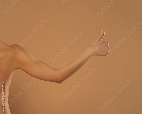 Young woman's stretched arm thumb up. Isolated on beige background