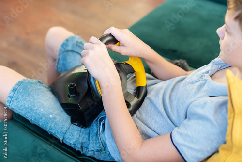 Teen boy gamer playing racing games on the computer. He uses the steering wheel. Getting ready for professional driving. Stimulation driving, child playing video game