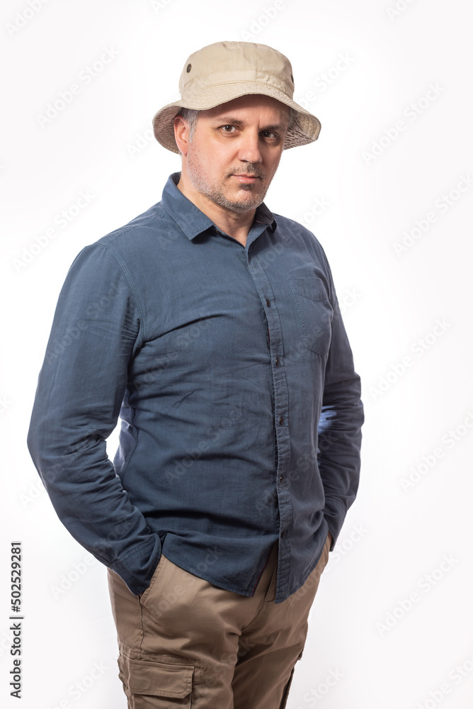 Portrait of a bearded middle-aged man in khaki trousers and hat looking thoughtfully at the camera over a white studio background with copy space Portrait of a bearded middle-aged man in khaki trousers and hat looking thoughtfully at the camera over a white studio background with copy space