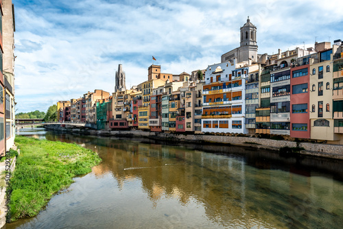 Colorful yellow and orange houses reflected in water river Onyar, in Girona, Catalonia, Spain. Church of Sant Feliu and Saint Mary Cathedral at background.