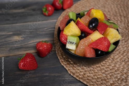 Fresh fruit salad  top view in a bowl on wooden background  vegetarian food concept