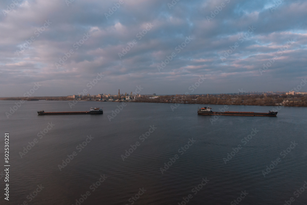 The cargo ship arrives at the river port. View from above. Panoramic view of the city. Barge floating on the Dnieper River, Ukraine. Bird's-eye view.