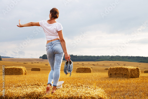 barefoot girl with sneakers in hand stands on a haystack on a bale in the agricultural field after harvesting © stopabox