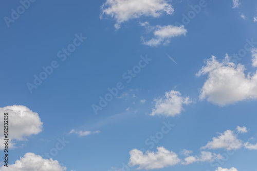 Fluffy isolated white clouds on a pale blue summer midday sky, ideal background, copy space