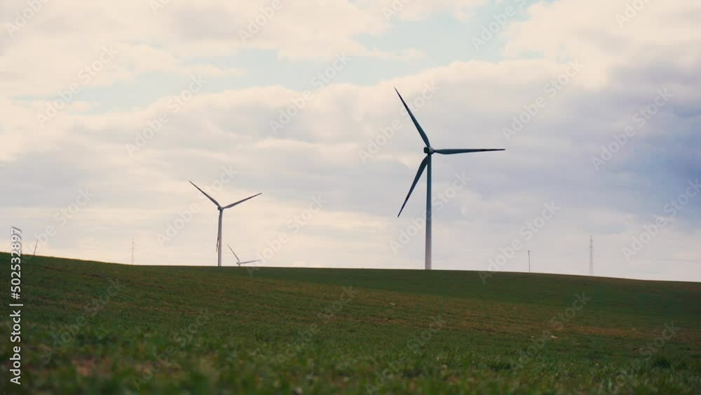 Large wind turbines under rainy cloudy sky with rotating blades in agriculture field with growing wheat in evening. Electricity saving and concept of alternative power source Large wind turbines under rainy cloudy sky with rotating blades in agriculture field with growing wheat in evening. Electricity saving and concept of alternative power source