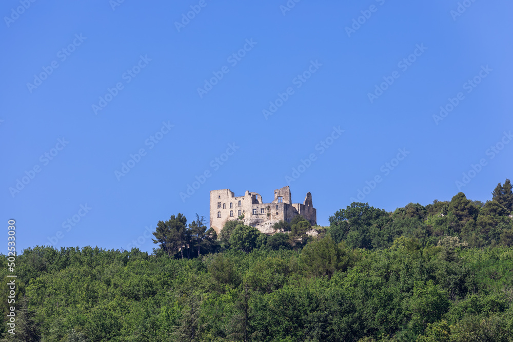 Intimidating ruins of Lacoste castle, also known as castle of Marquis de Sade, on hill among dense foliage of surrounding forest against clear blue sky. Vaucluse, Provence, France