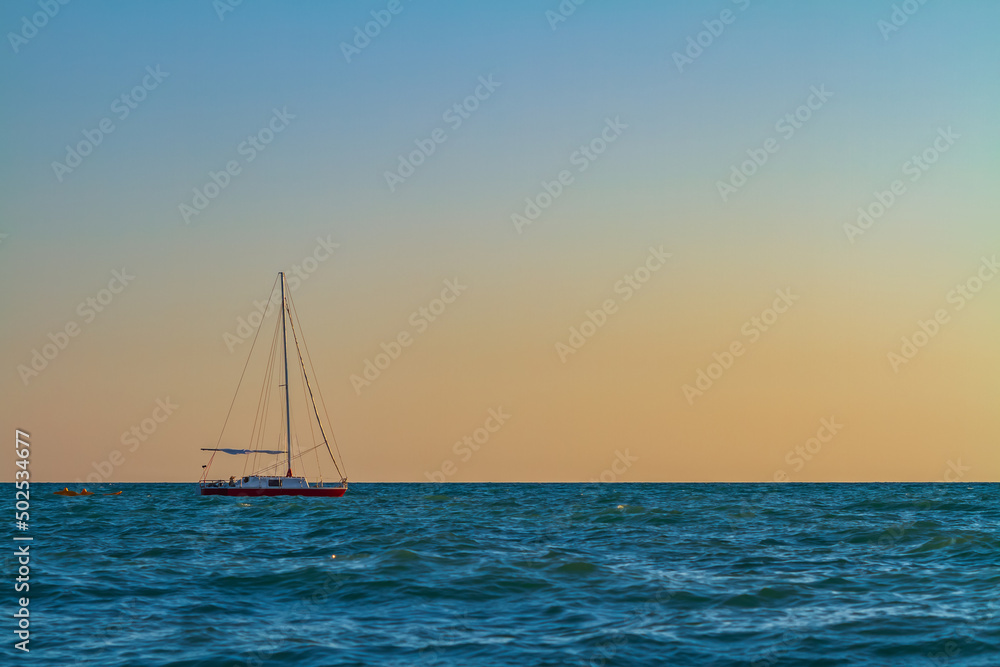 A small sailboat floats in the sea at sunset