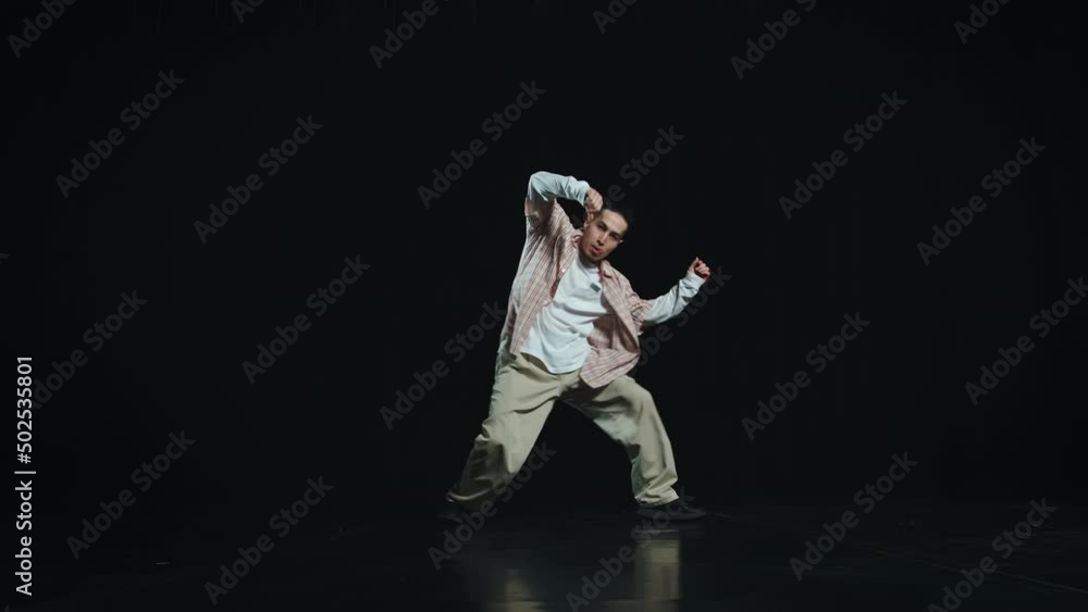 The guy in white loose clothes dances hip hop cool. He constantly moves, crouches, and rotates his legs. Then he sits down and shakes his shoulders The guy in white loose clothes dances hip hop cool. He constantly moves, crouches, and rotates his legs. Then he sits down and shakes his shoulders