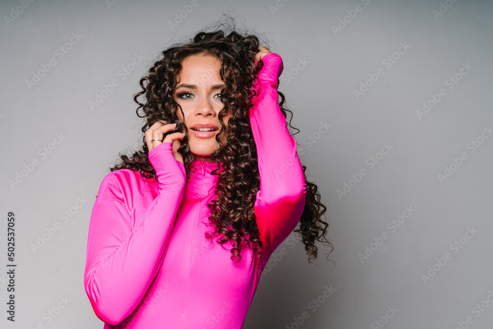 The girl is an athlete in a bright pink fused swimsuit with long sleeves. A student with dark long curly hair looks into the camera. Portrait of a cheerleader close-up on a white background. An The girl is an athlete in a bright pink fused swimsuit with long sleeves. A student with dark long curly hair looks into the camera. Portrait of a cheerleader close-up on a white background. An