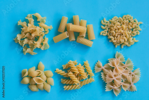 Various kinds of uncooked pasta on the blue background, top view. Collection of different raw pasta on cooking table