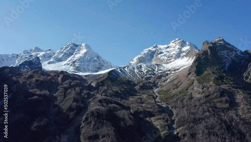 Drone flying along snow covered white mountain glacier in sunny autumn day, Tuymazinsky glacier, Digoriya gorge, Northern Ossetia - Alania, Caucasus, Russia