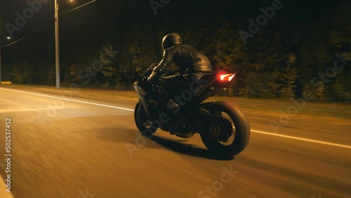 Young man in helmet riding fast on modern black sport motorbike at evening city street. Motorcyclist racing his motorcycle on night empty road. Guy driving bike. Concept of freedom and hobby. Close up